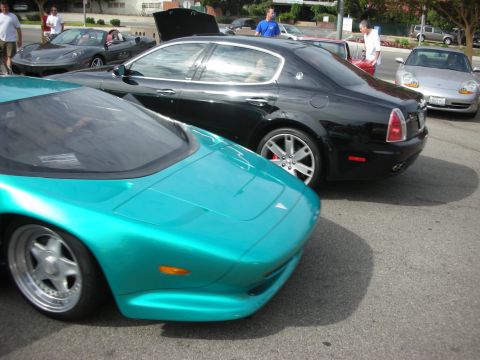 1998 Ford Crown Victoria - A teal sports car is parked in front of a black Maserati, with other vehicles visible in the background at a car meet.