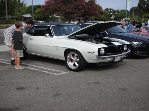 1998 Ford Crown Victoria - A father and son look at a classic white 1969 Chevrolet Camaro Z/28 with its hood open at a car meet.