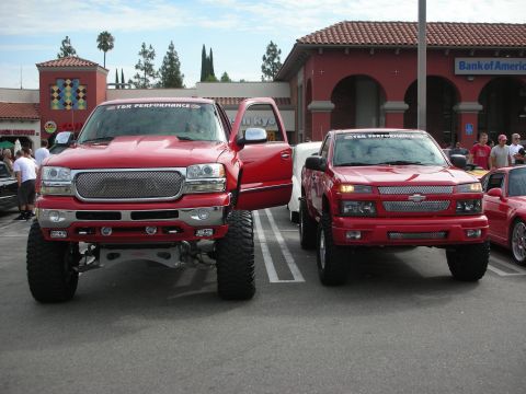 1998 Ford Crown Victoria - Two modified red pickup trucks are parked side-by-side in a parking lot.