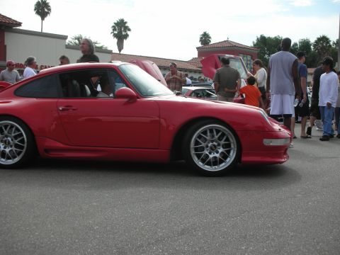 1998 Ford Crown Victoria - A red Porsche 911 is the focus of this outdoor car meet, with several people observing.