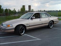 1993 Ford Crown Victoria - A tan/champagne 1990s Ford Crown Victoria full-size sedan shown from a front three-quarter angle, fitted with aftermarket chrome multi-spok…