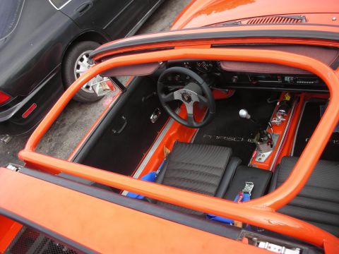 1998 Ford Crown Victoria - The interior of an orange sports car, racing seats, a roll cage, and Porsche branded floor mats, is visible next to a black car.