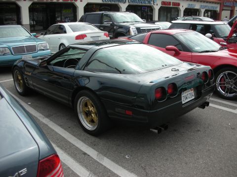 1998 Ford Crown Victoria - A dark green Chevrolet Corvette C4 with gold rims is parked in a lot, seen from the rear.