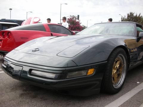 1998 Ford Crown Victoria - dark green Chevrolet Corvette with gold mesh wheels sits in a parking lot, a red sports car visible beside it.