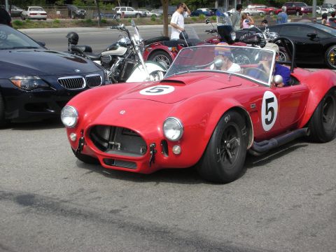 1998 Ford Crown Victoria - red Shelby Cobra-style roadster wearing race number 5 sits in a parking lot with motorcycles and a black BMW behind it.