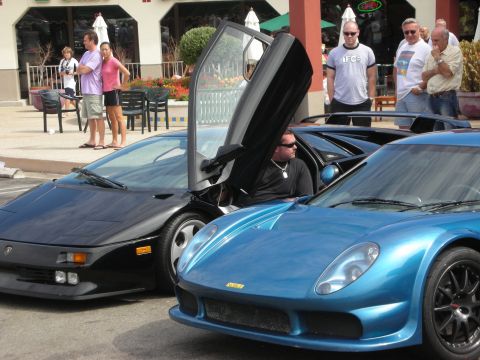 1998 Ford Crown Victoria - black Lamborghini Diablo with its scissor door up sits next to a blue supercar as onlookers watch at a car show.