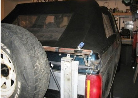 1995 Ford Bronco - This dark blue SUV features a soft top and a spare tire mounted on its side, seen from the rear.