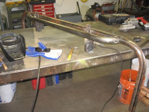 1991 Ford Bronco - A custom metal rear bumper is in progress on a workbench, surrounded by fabrication tools and safety equipment.