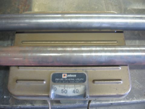 1991 Ford Bronco - Metal pipes are weighed on a general utility scale, indicating a measurement around 50 pounds.