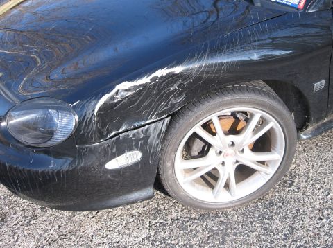 1999 Ford Taurus - The front fender of a black car shows significant damage with white paint scraped across the surface.