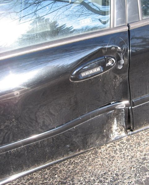 1999 Ford Taurus - Damage to the side of a black car, including the door and handle, is visible.