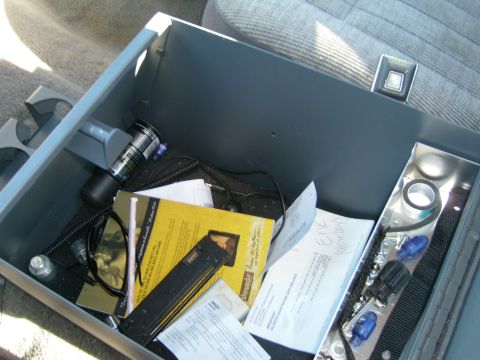 1989 Ford Bronco - Interior view of a vehicle's center console storage bin containing various items.