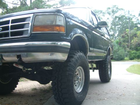 1992 Ford Bronco - A lifted 1992 Ford Bronco is shown from a low angle, highlighting its large tires and front grille.