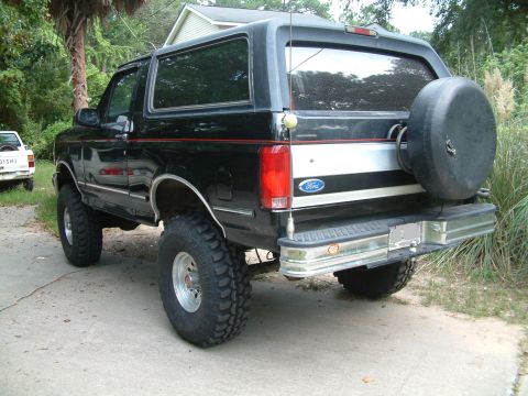1992 Ford Bronco - This black Ford Bronco is parked on a concrete driveway with a white Mitsubishi pickup truck in the background.