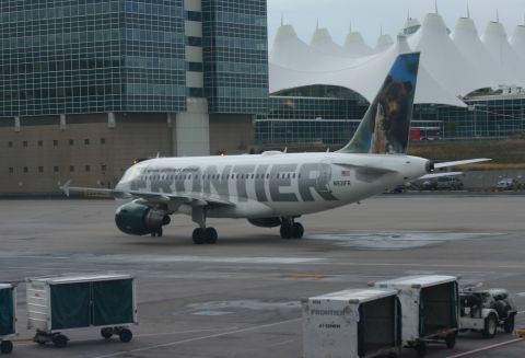 1997 Ford Probe - A Frontier Airlines jet with a bear graphic on its tail is on the tarmac near airport buildings and baggage carts.