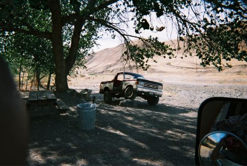 1991 Ford Bronco - A two-tone Ford F-Series truck is parked on a dirt lot with a hilly, arid landscape in the background.
