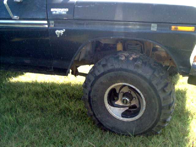 Lifted dark Ford Bronco front fender with large mud tire on black aluminum wheel, parked on grass