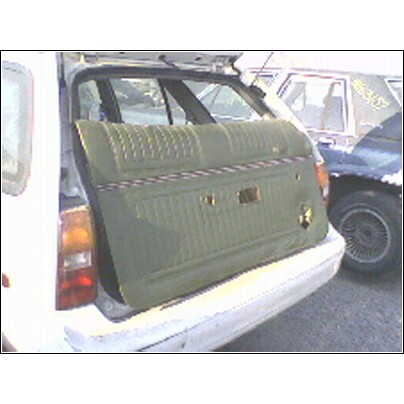 1973 Ford Ranchero - A green car door panel is placed on the bumper of a white car, with another vehicle visible behind.