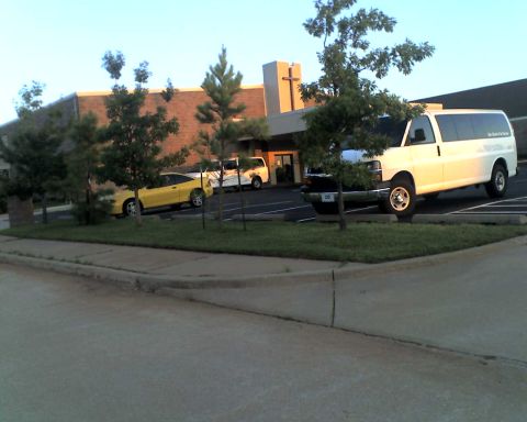 1965 Ford Mustang - A white van and a yellow car are parked in front of a building with a cross on top.