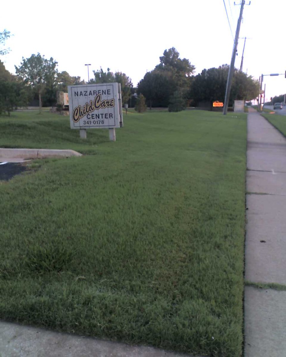 Sign for Nazarene Child Care Center with phone number 341-0178. Sidewalk and grass in foreground, trees and street in background