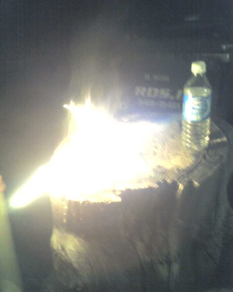 1965 Ford Mustang - A bottle of water sits beside a stump engulfed in flames, with faint text in the dark background.