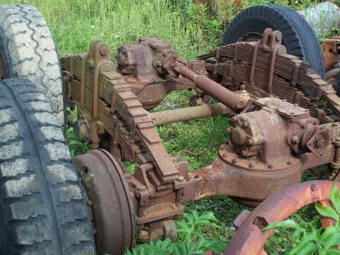 1979 Ford F-150 - Close-up of a heavily rusted truck rear axle assembly, showing leaf springs and large tires, suggesting a heavy-duty vehicle.