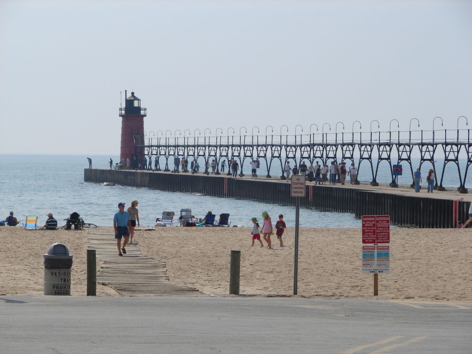 Red lighthouse and pier on Lake Michigan beach with people walking