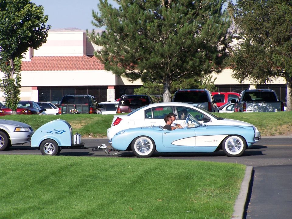 Light blue and white convertible with a trailer driving on a road