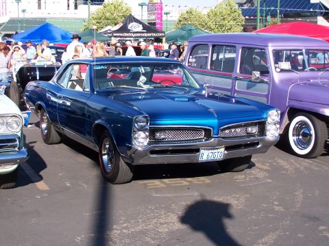 1990 Ford Bronco - A blue 1967 Pontiac GTO is parked next to a purple woodie wagon at an outdoor car show.