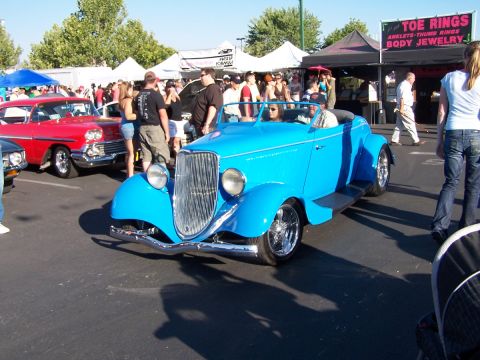 1990 Ford Bronco - A bright blue convertible hot rod is displayed at an outdoor event with a red classic car in the background.