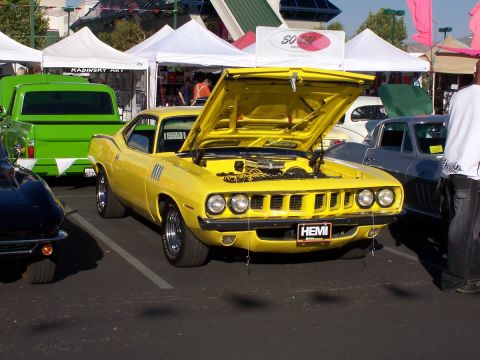 1990 Ford Bronco - Yellow 1970 Plymouth Barracuda at an outdoor car show, hood up to reveal engine.