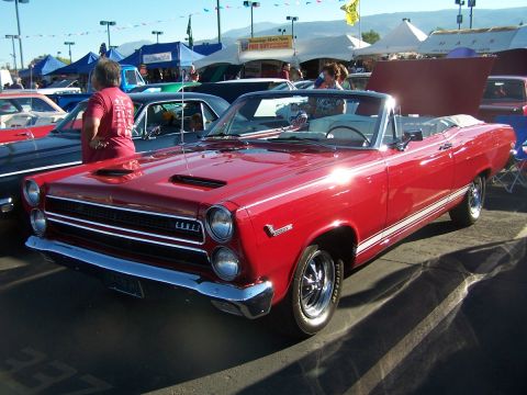 1990 Ford Bronco - A red convertible with white side stripes is parked at an outdoor car show.