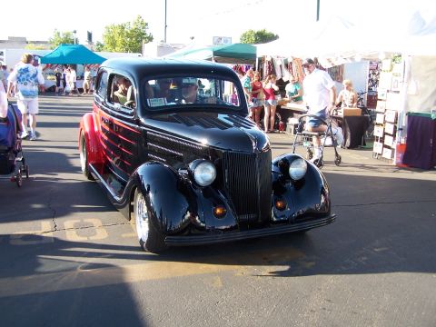 1990 Ford Bronco - A vintage black sedan with red accents is displayed at an outdoor event with vendors in the background.
