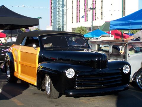 1990 Ford Bronco - A custom black convertible with wood paneling is displayed at an outdoor event.