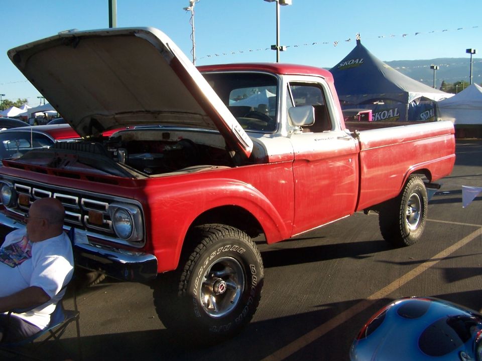 Red and white pickup truck with hood open, parked outdoors. Chrome grille and bumper visible