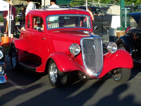 1990 Ford Bronco - A red coupe hot rod is parked at an outdoor event, with other vehicles visible in the background.