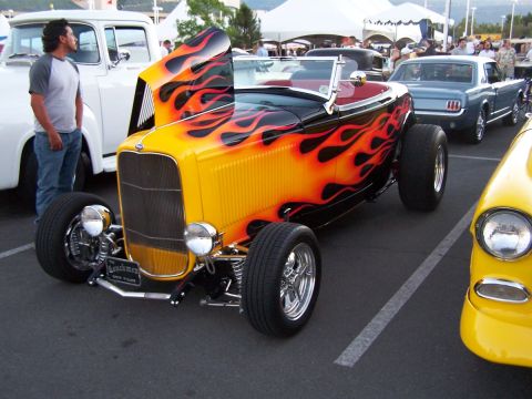 1990 Ford Bronco - A custom hot rod with a flame paint job is displayed at an outdoor car show.