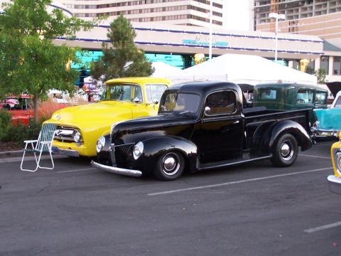 1990 Ford Bronco - A black pickup truck is parked in a lot with other vehicles, including a bright yellow truck.