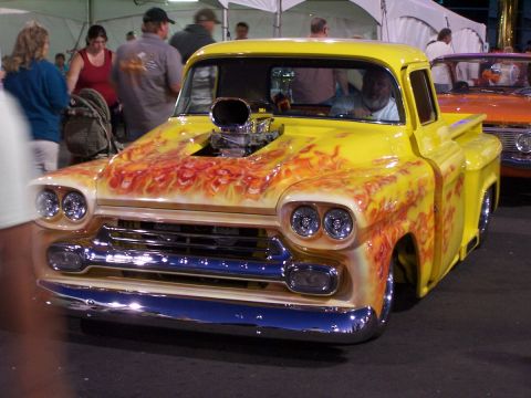 1990 Ford Bronco - A custom yellow pickup truck with flame graphics and a prominent blower is displayed at an event.
