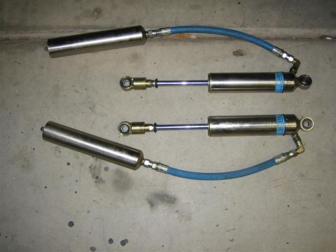 1987 Suzuki Samurai - Two silver shock absorbers with blue hoses and blue Bilstein labels are shown on a concrete surface.