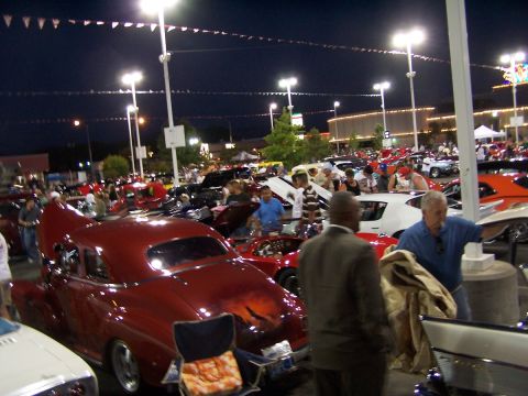 1990 Ford Bronco - A gathering of vehicles and people at an outdoor event under bright lights at night.