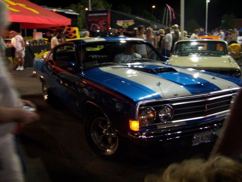 1990 Ford Bronco - A blue and white 1970 Ford Torino GT is on display at an outdoor car show with other vehicles and people around.