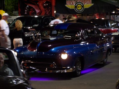 1990 Ford Bronco - A customized coupe with a striking two-tone paint job and vibrant purple underglow is displayed at a car show.