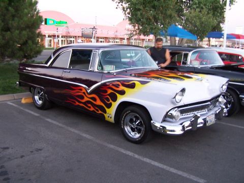 1990 Ford Bronco - A customized 1955 Ford Fairlane Crown Victoria with flame graphics is parked next to another vehicle.