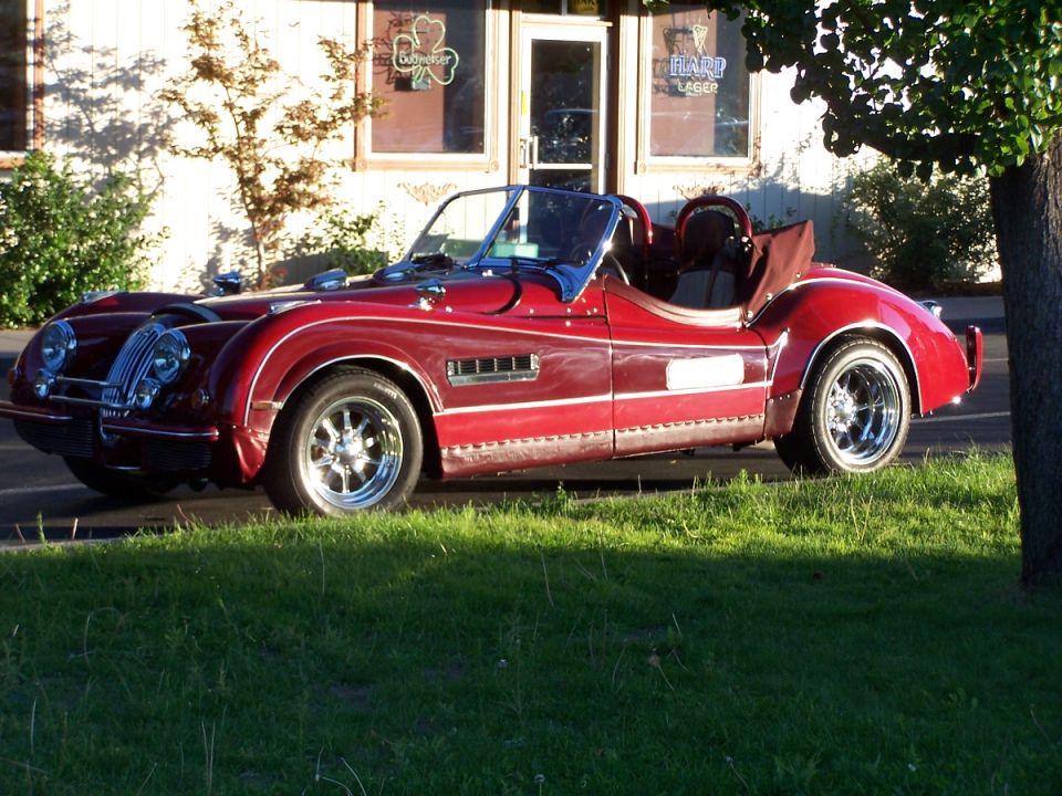 Red convertible sports car with chrome accents and wire wheels parked on grass