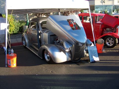 1990 Ford Bronco - A silver custom coupe with its hood open is displayed next to a red sedan at an outdoor event.