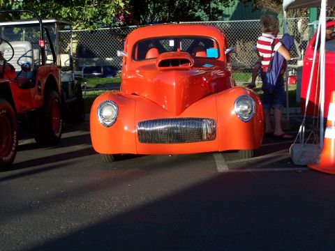 1990 Ford Bronco - An orange hot rod coupe is parked next to a red Jeep at an outdoor event.