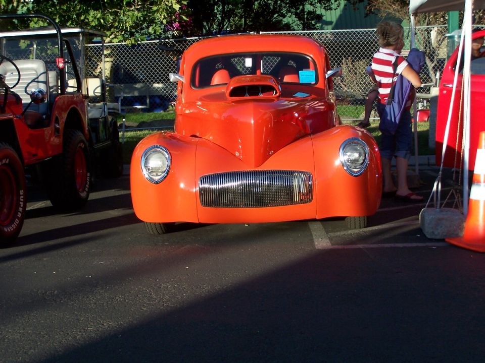 Orange hot rod coupe with a chrome grille and hood scoop, parked next to a red Jeep