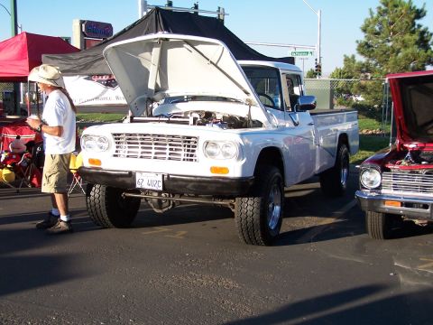 1990 Ford Bronco - A white pickup truck is displayed with its hood open, parked next to another vehicle at an outdoor event.