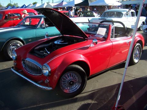 1990 Ford Bronco - A red convertible sports car is displayed with its hood open at an outdoor car show.